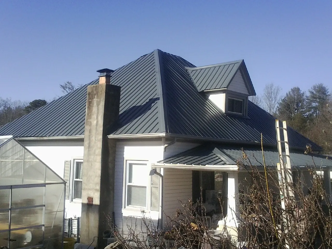 Dark blue standing seam metal roof on a white farmhouse with dormer in Manchester